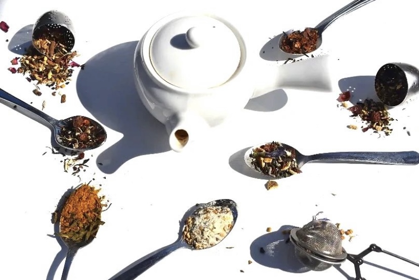 A white teapot and spoons with different types of food on them.